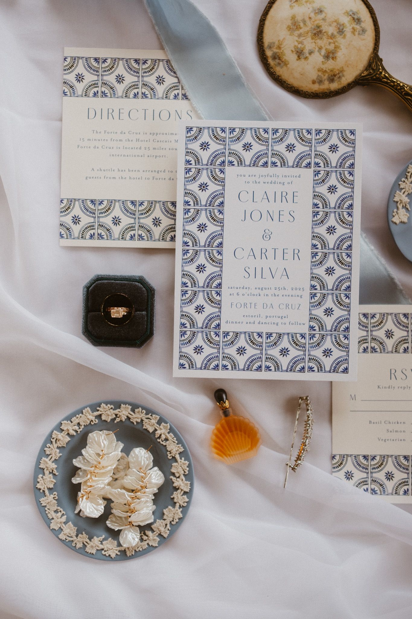 Wedding stationery and decorative items arranged on white fabric with blue and white patterned design.