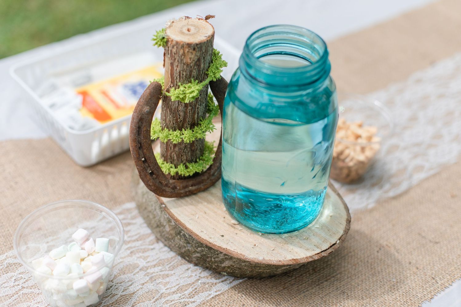Blue mason jar centerpiece with moss on rustic wood slice table decor.