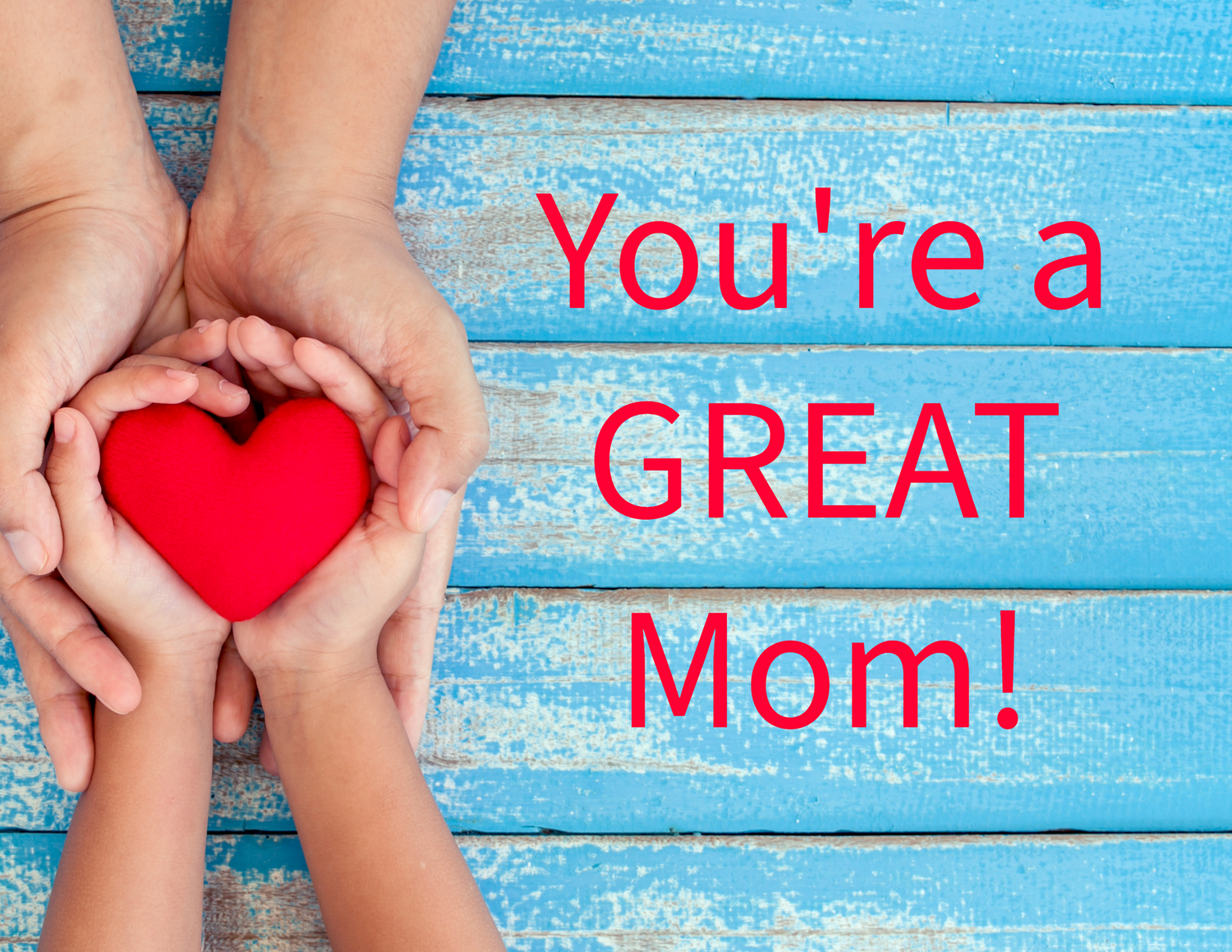 Hands holding red heart shape with motivational text about motherhood on blue wooden background.
