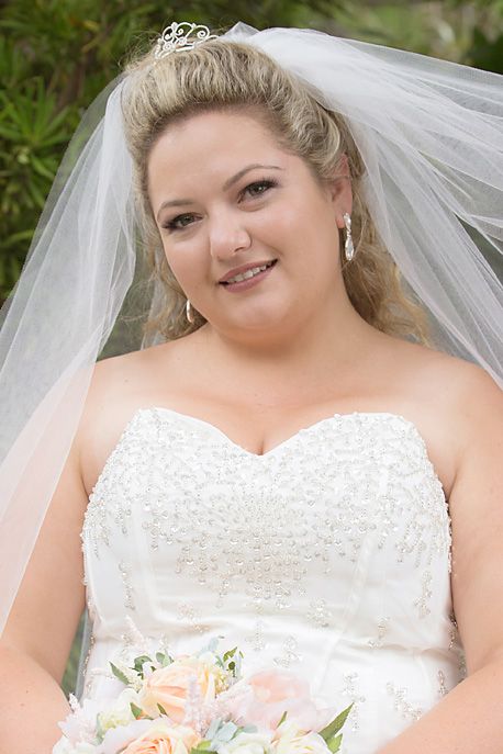 Bride in white strapless wedding dress wearing veil and holding peach bouquet poses for photos outdoors.