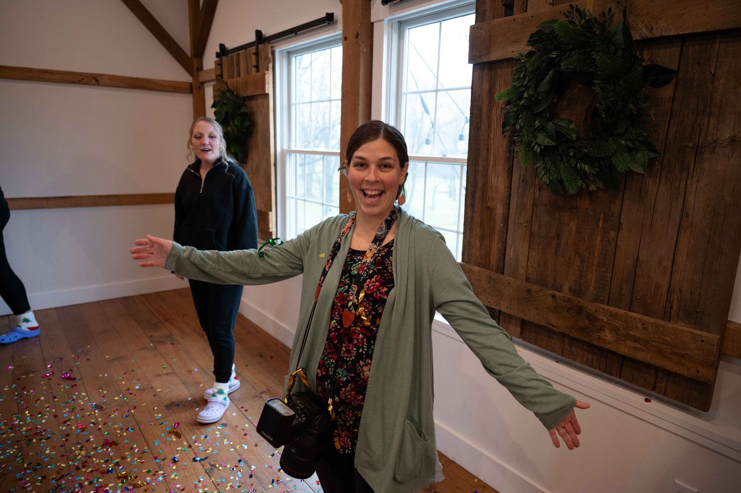 Someone with outstretched arms stands in a rustic room with wooden beams and confetti on the floor.