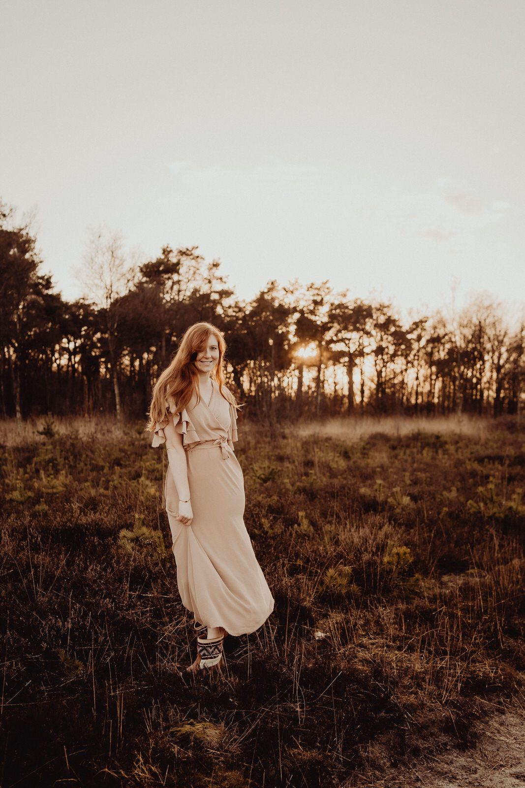 Woman in light dress standing in field during golden sunset.