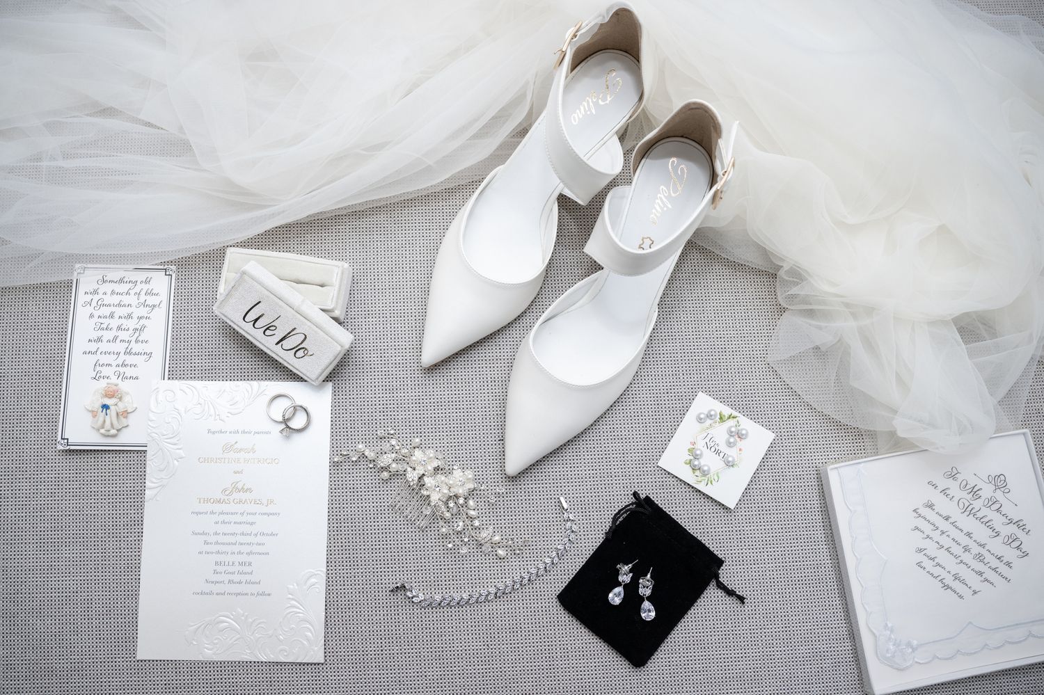 White bridal shoes arranged with wedding invitations, jewelry and accessories on tulle fabric.