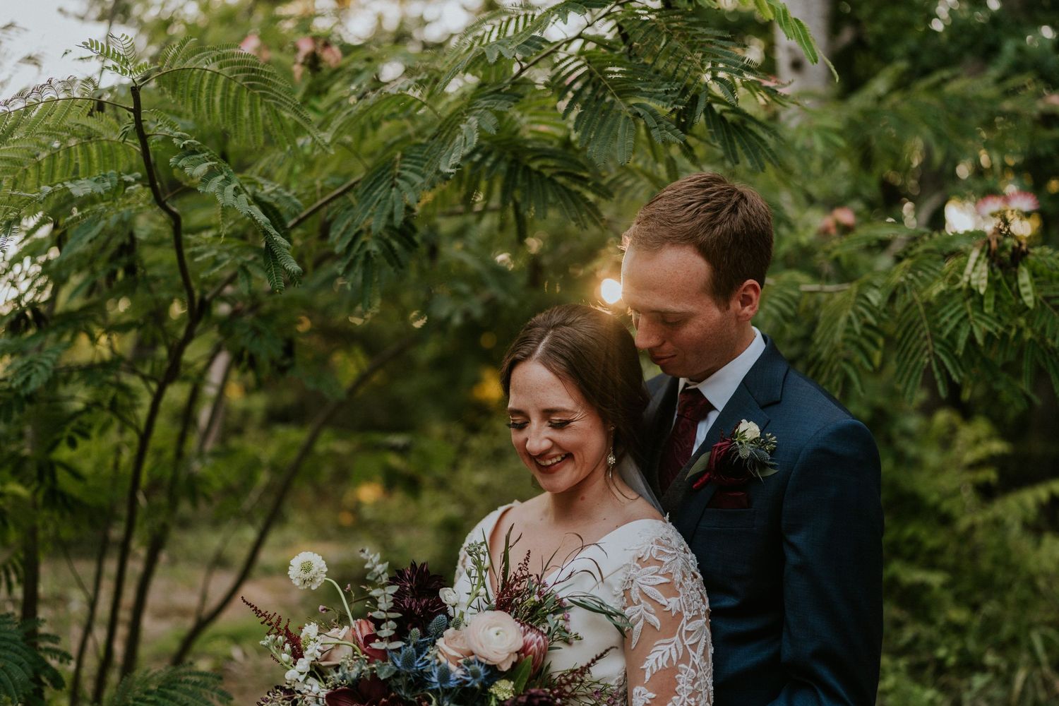 A couple shares an intimate moment in a garden setting with a beautiful bouquet.