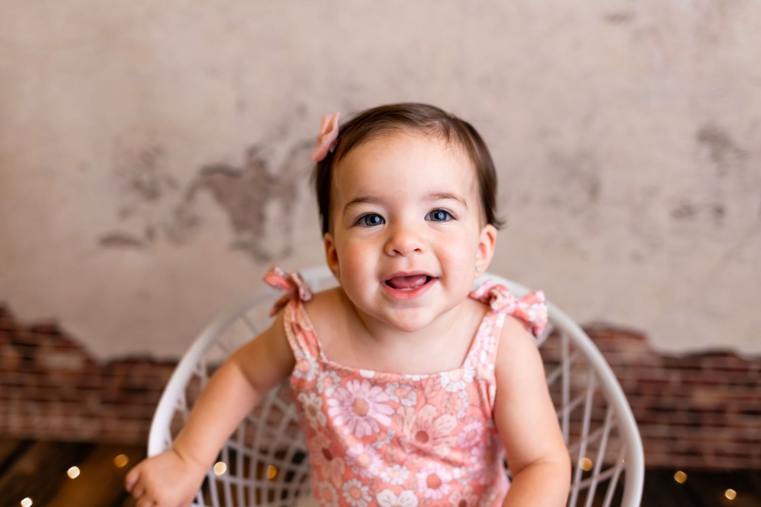 Happy baby in pink outfit sitting in vintage-style chair against distressed wall background.