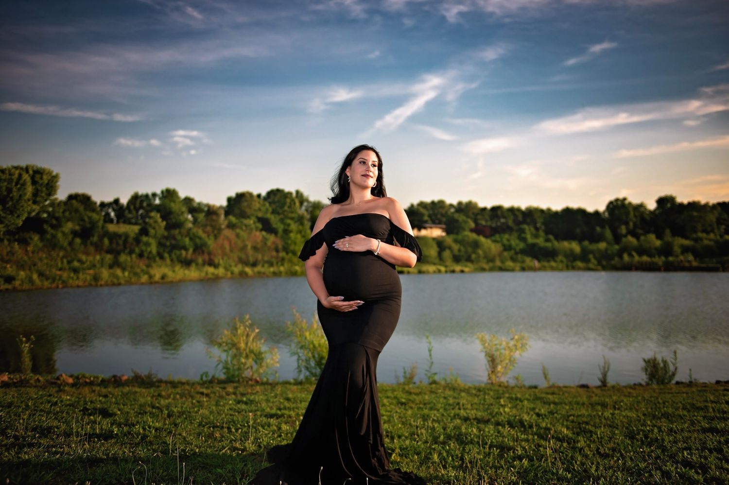 A maternity photoshoot at sunset by a lake with a black flowing dress.