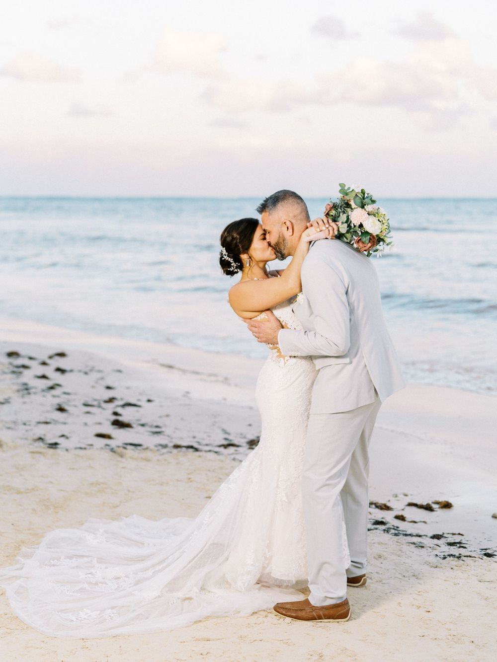 Newlyweds share a romantic kiss on a tropical beach at sunset.