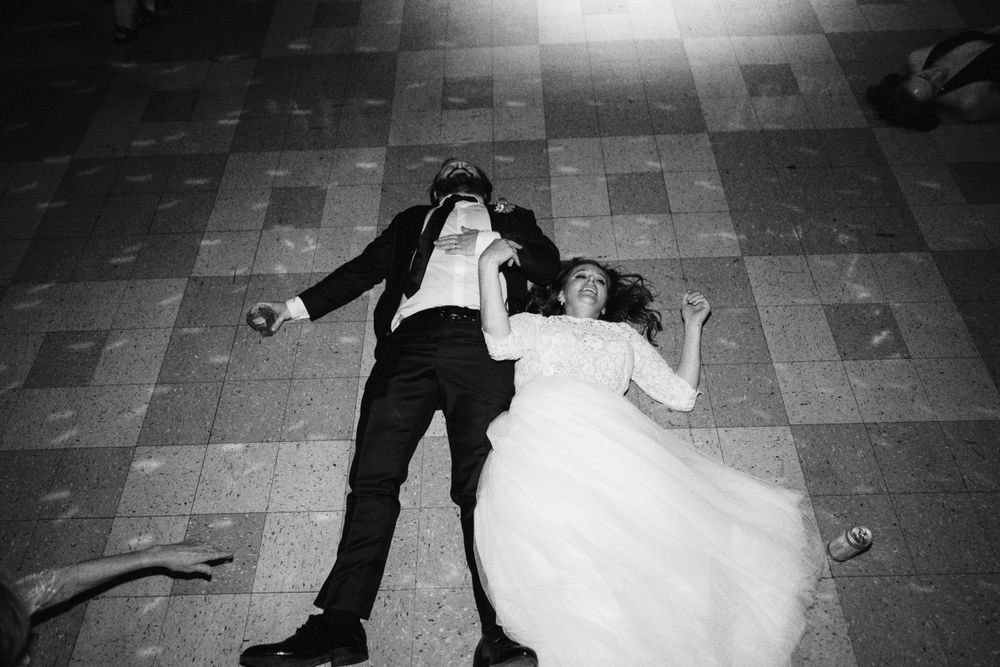 Dramatic black and white shot of couple laying on floor during wedding reception.