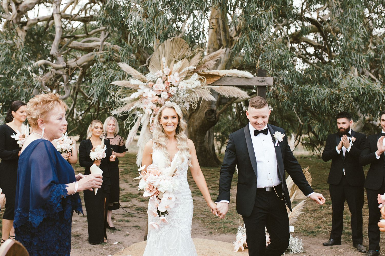 Wedding party and guests celebrating outdoors under eucalyptus trees at garden ceremony.