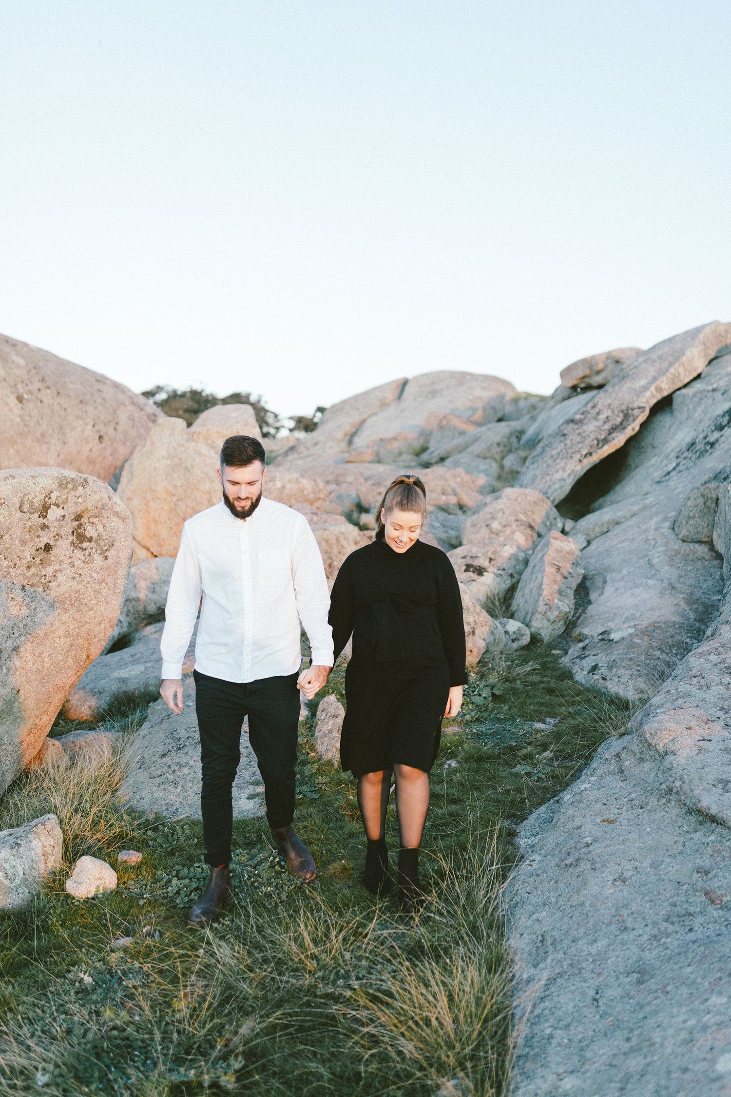 Couple walking down rocky slope with grass patches.