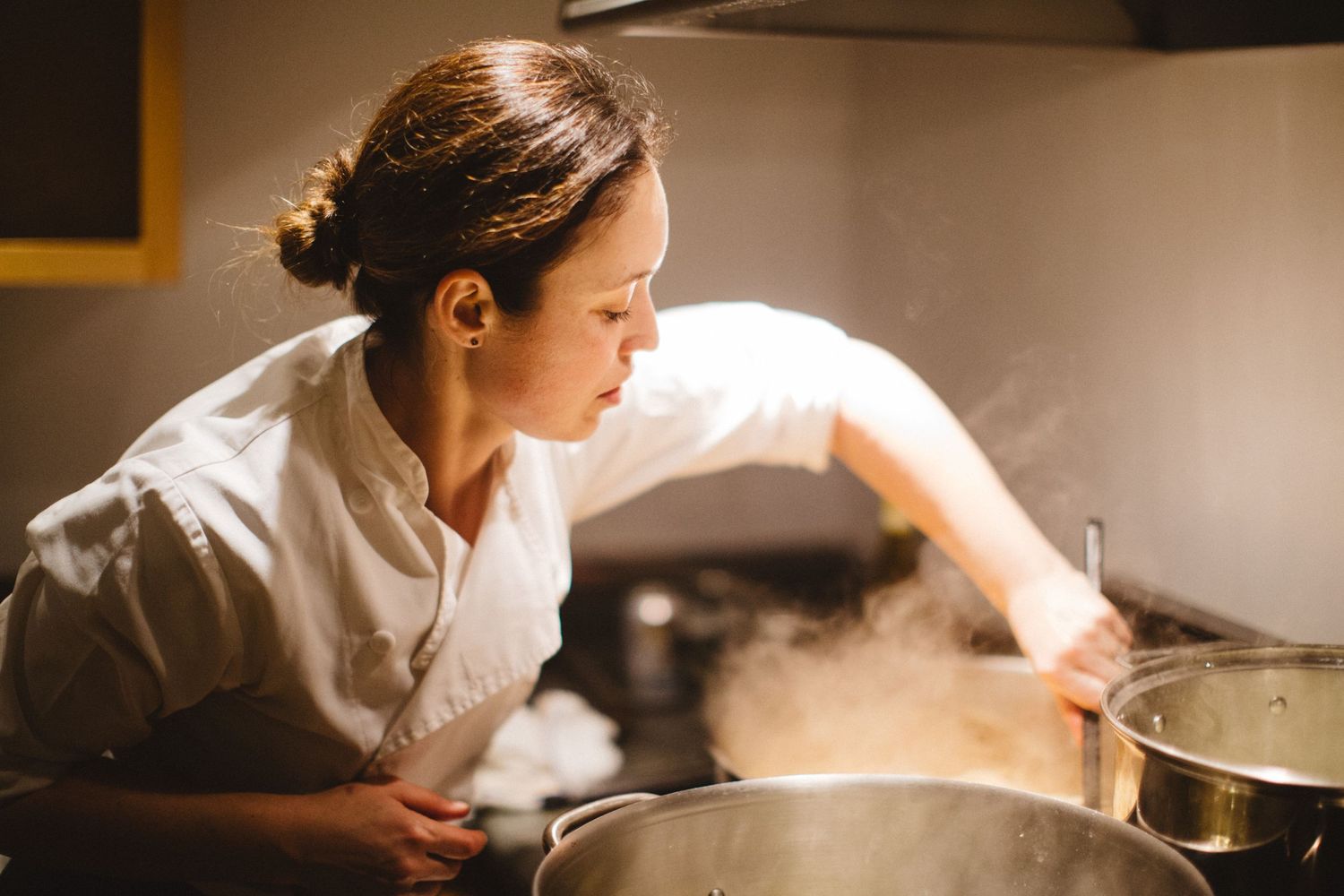 Chef in white uniform checking steaming pots in a professional kitchen.