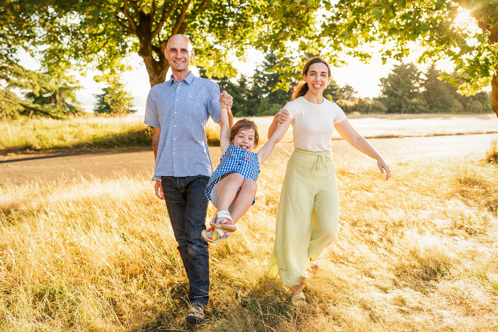 Parents swinging their daughter among the tall grasses at sunset in Discovery Park.