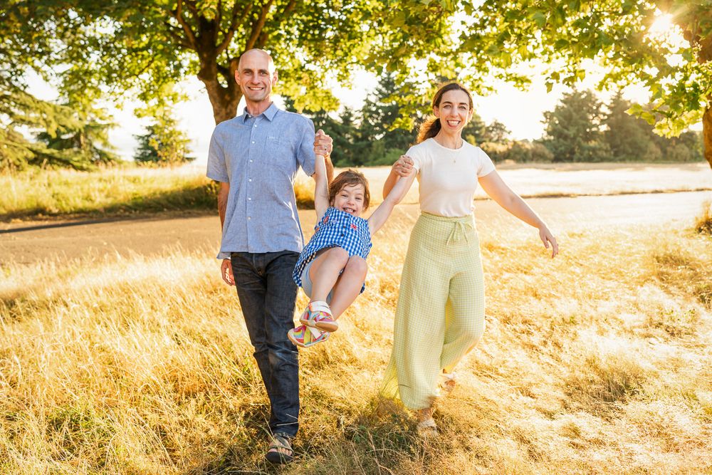 Parents swinging their daughter among the tall grasses at sunset in Discovery Park.