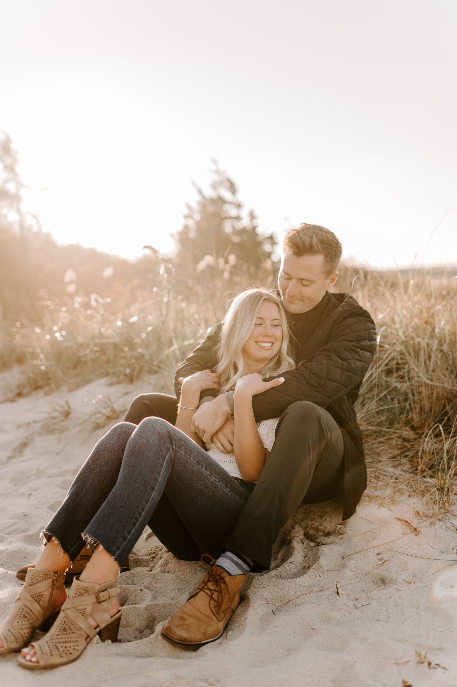 Couple laughing while lying on sandy beach during golden hour sunset.