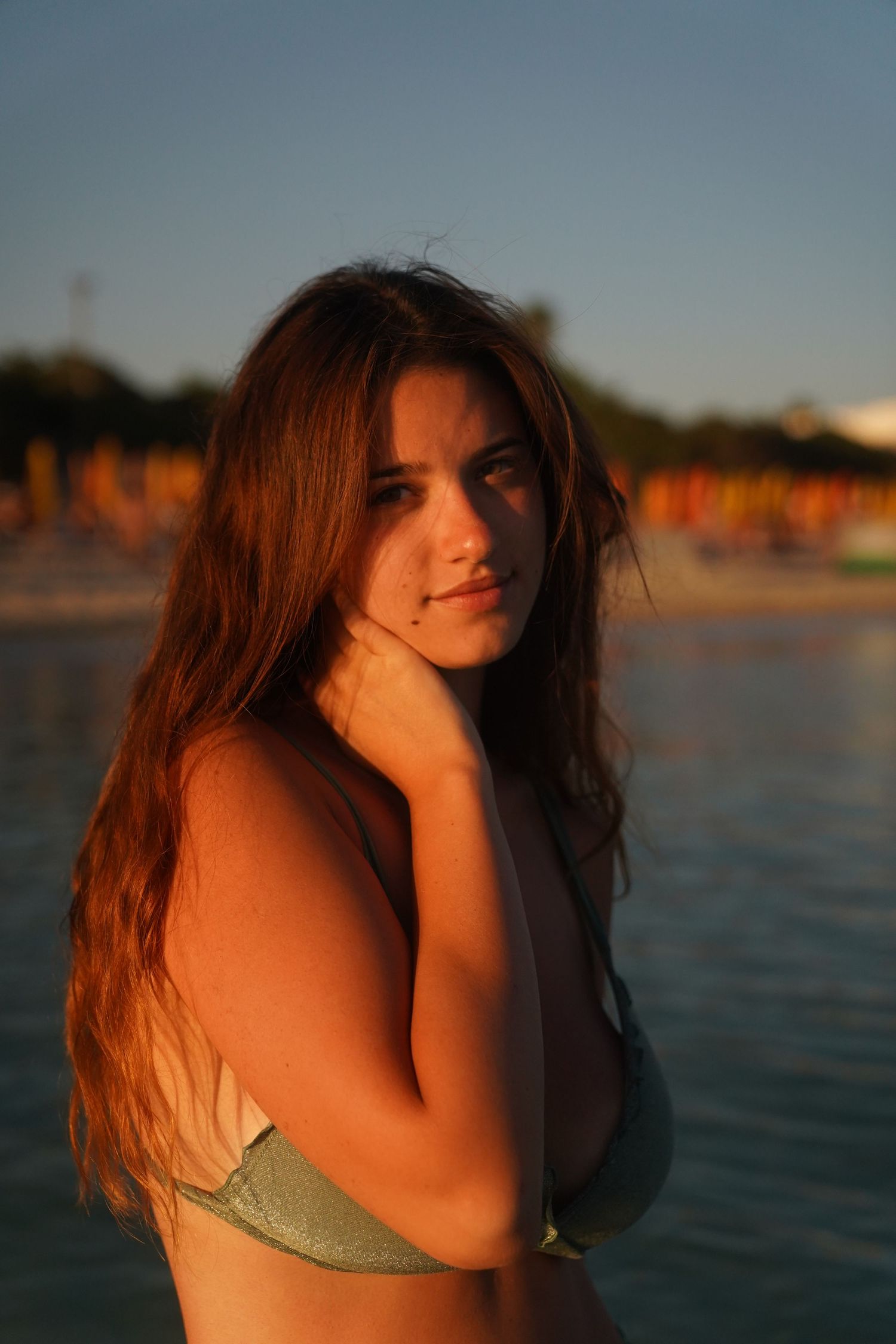 Beach portrait at golden hour showing woman in green swimwear with long dark hair against water backdrop.