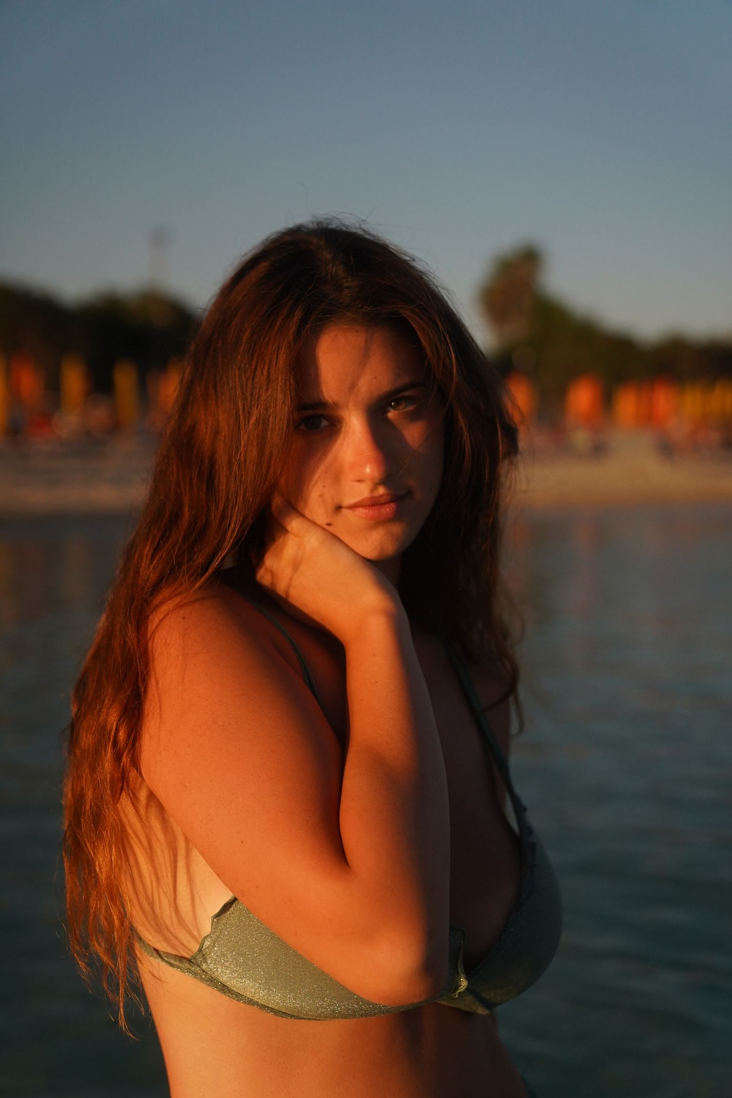 Closeup beach portrait during sunset showing woman in sage green bikini with flowing brown hair.