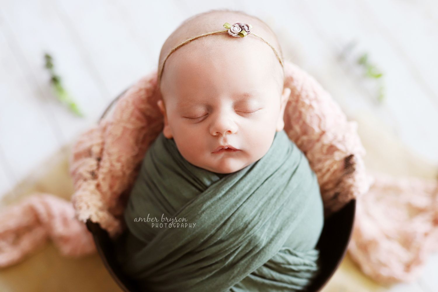 Sleeping newborn in sage green wrap with delicate headband.