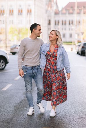 A smiling couple walks hand in hand down a city street, the woman wearing a floral dress and denim jacket.
