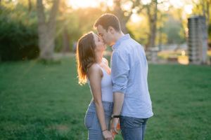 Young couple sharing a tender almost-kiss in a sunlit green park during golden hour.
