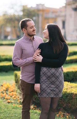 A couple shares a tender moment in a garden, the man embracing the woman as they smile at each other.