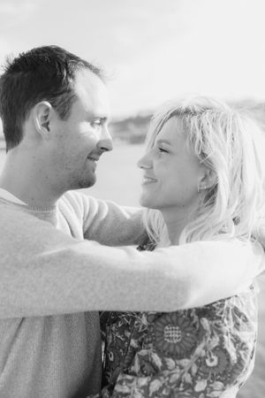A black and white close-up of a couple embracing and smiling at each other in an outdoor setting.