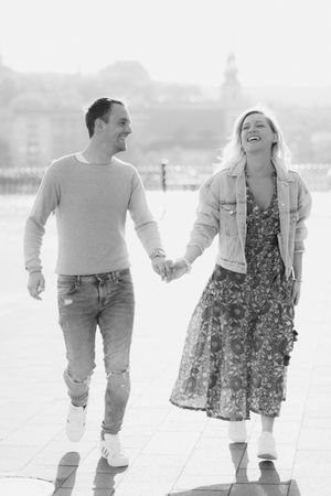 A black and white photo of a laughing couple holding hands and walking together on an open plaza.