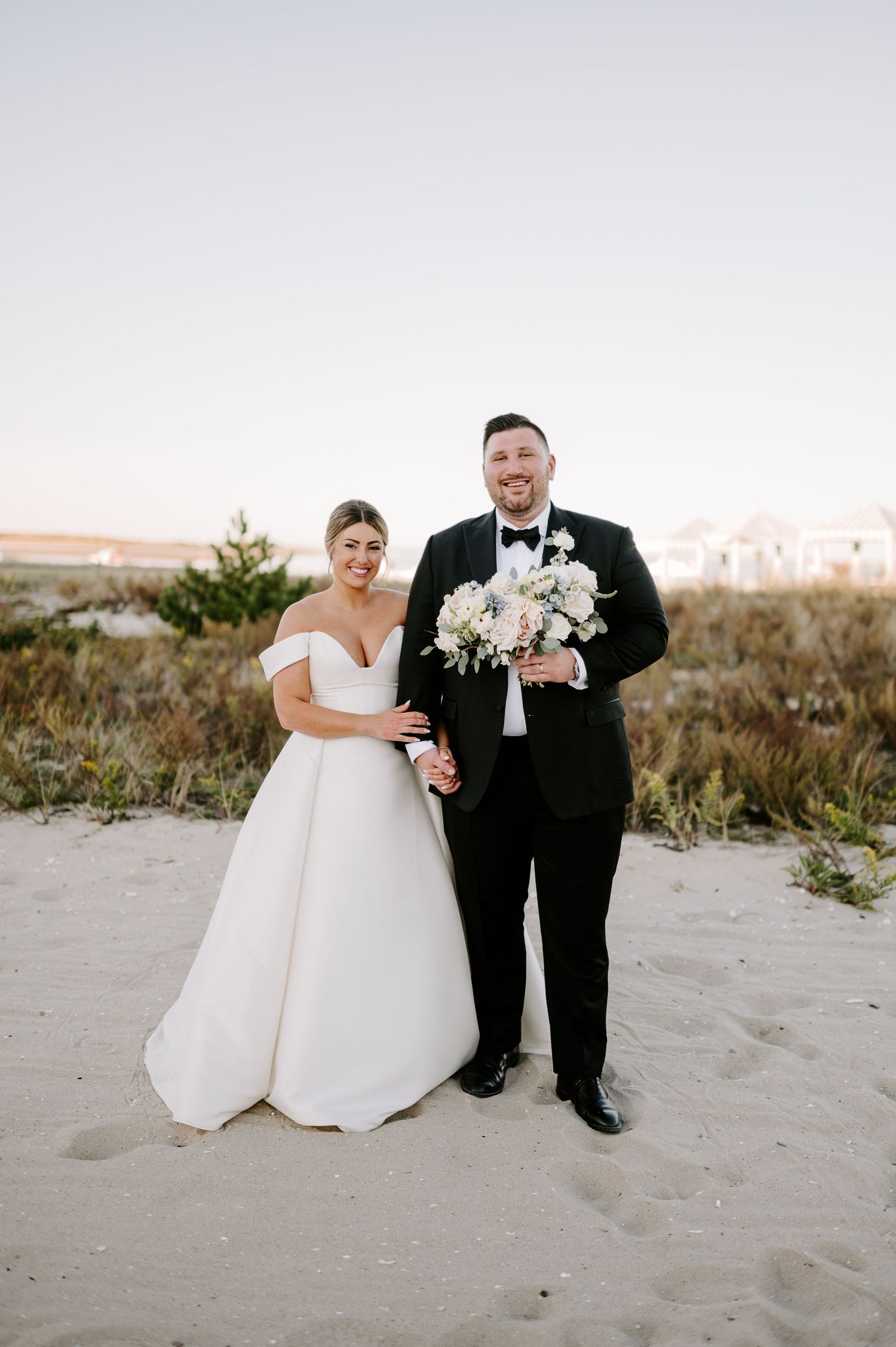 A bride and groom share an intimate moment on a sandy beach during their wedding photoshoot at sunset.