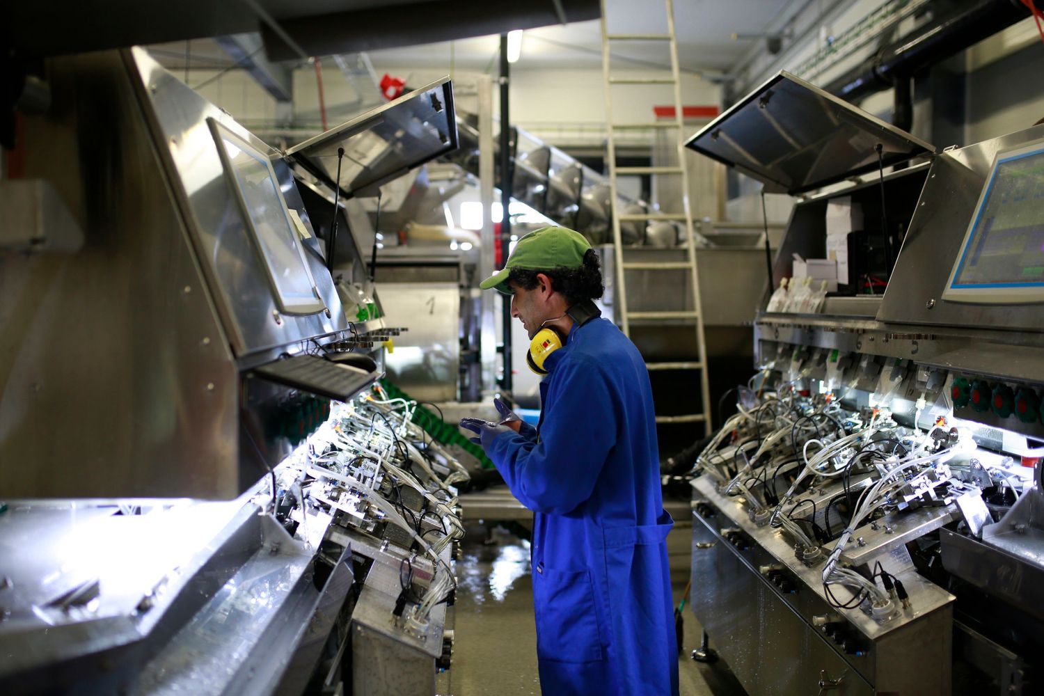 Industrial workspace with machinery and equipment being monitored by worker in protective gear.