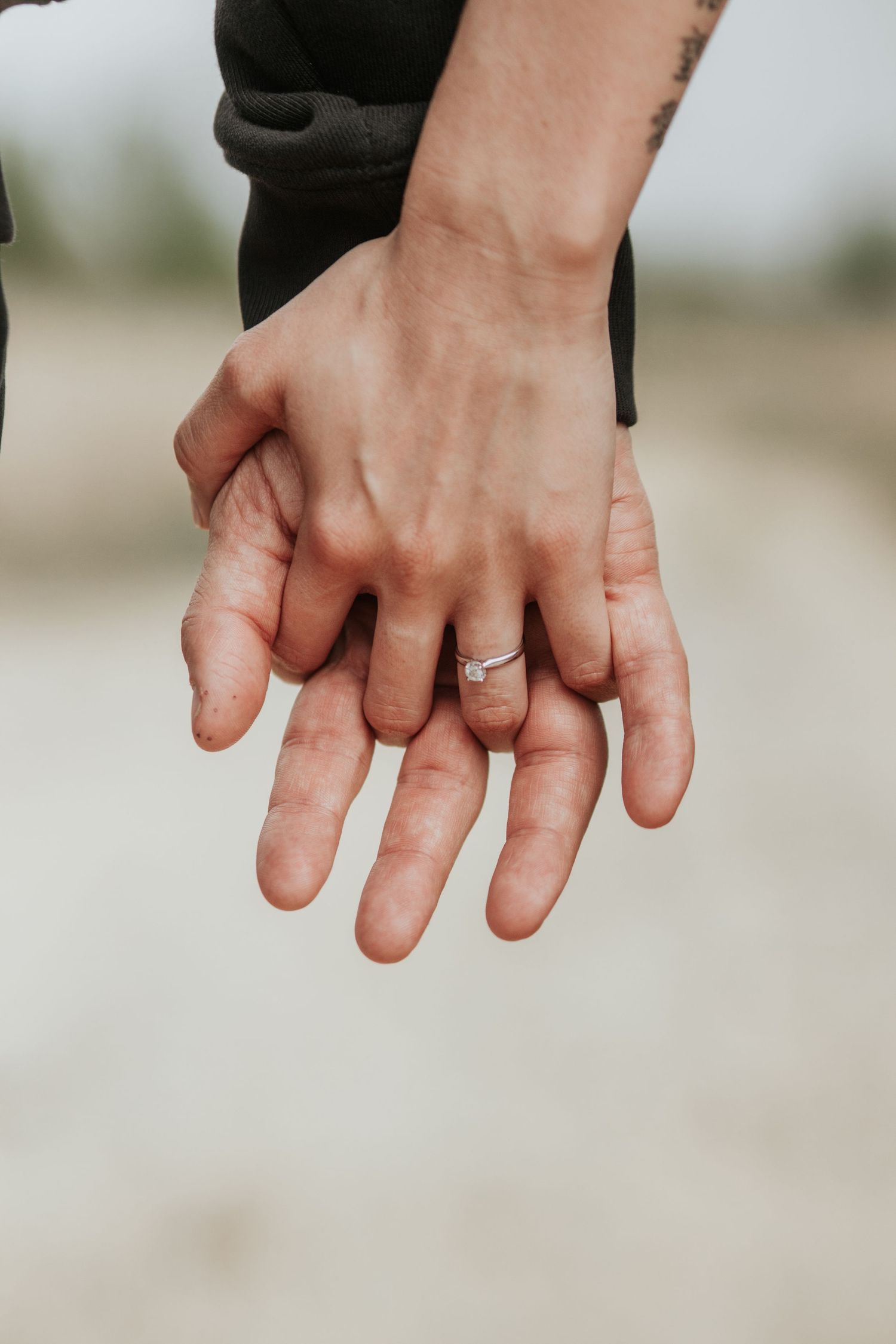 Close up of two hands clasped together showing a wedding ring against a blurred background.