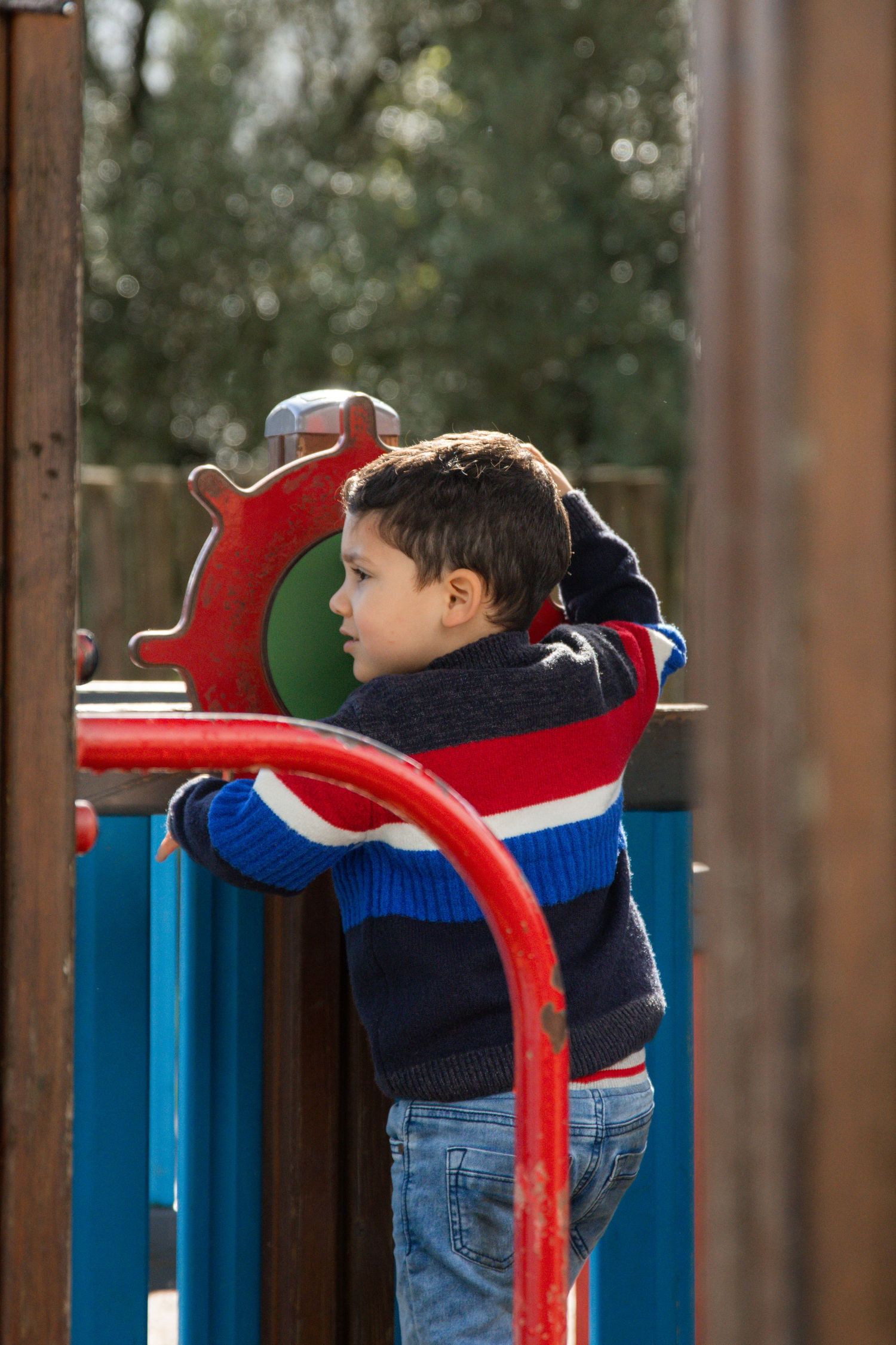 Child leans over blue playground equipment with a red scarf.