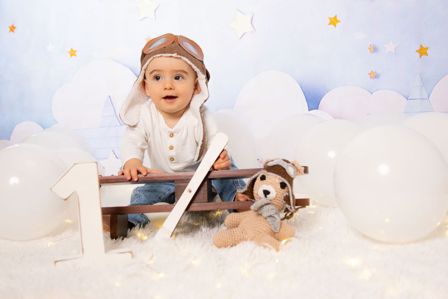 Baby photoshoot with plush toys and white clouds backdrop.