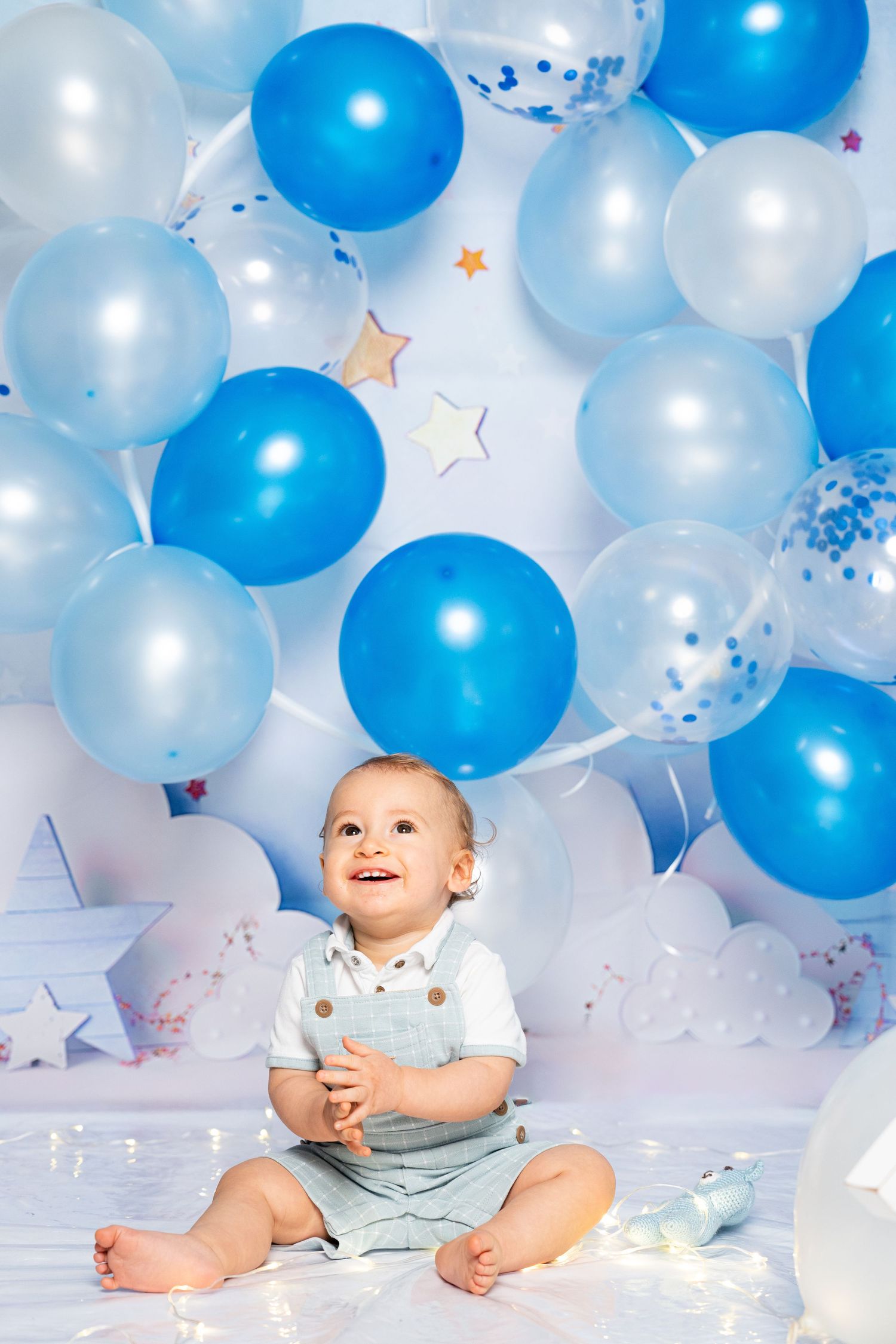 Smiling baby surrounded by blue and white balloons and star decorations in a studio setting.