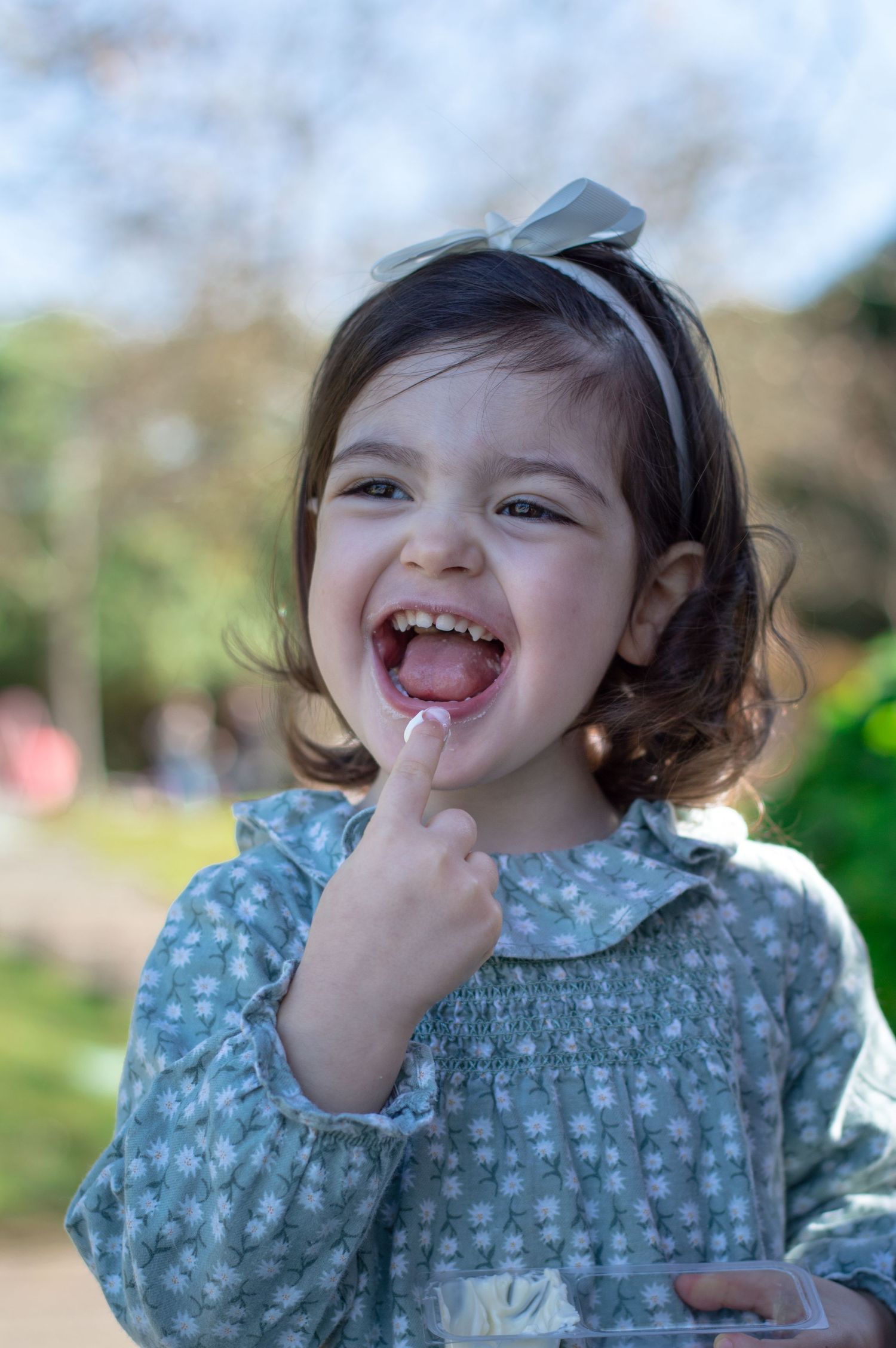 Child wearing blue polka dot dress laughing joyfully outdoors.
