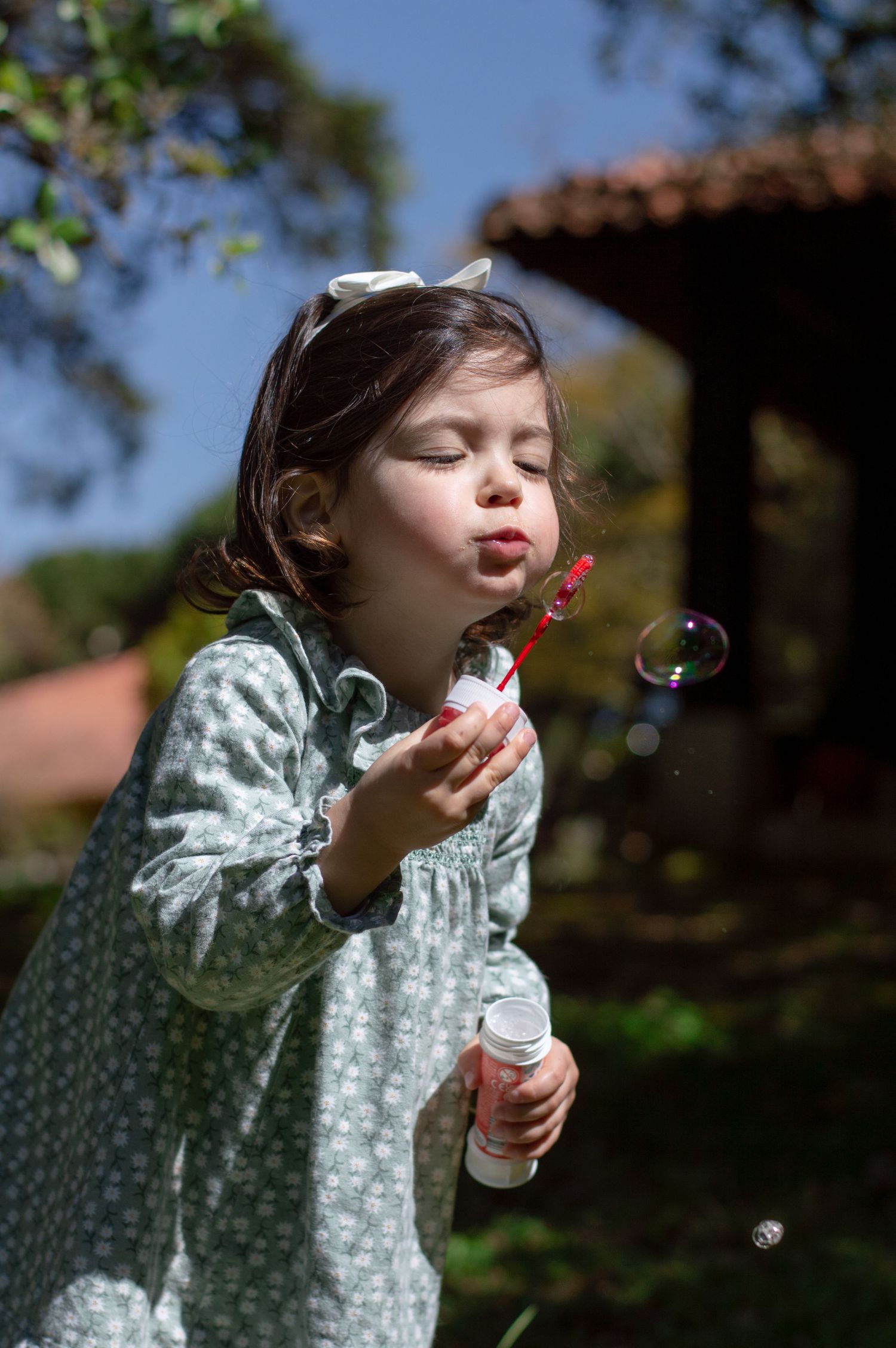 Child in polka dot dress blowing bubbles in a sunny garden.