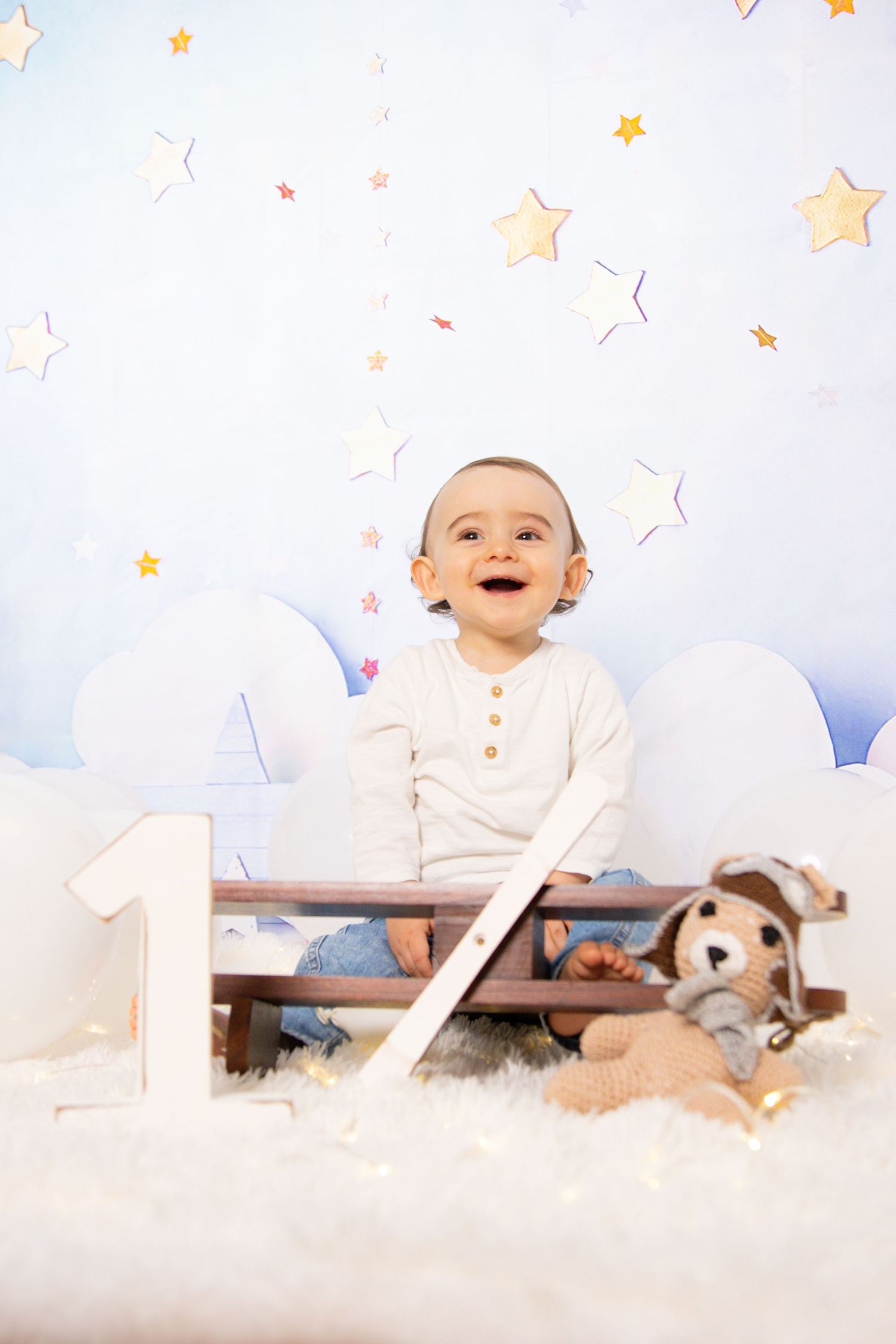Smiling baby playing with number one prop among stars and clouds.
