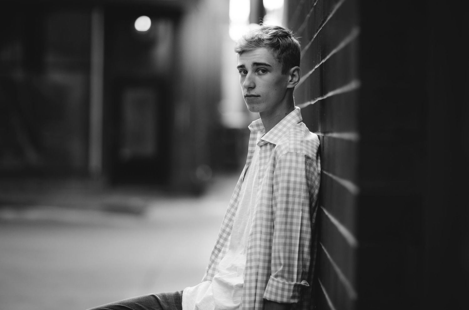 Black and white portrait against brick wall in moody lighting.