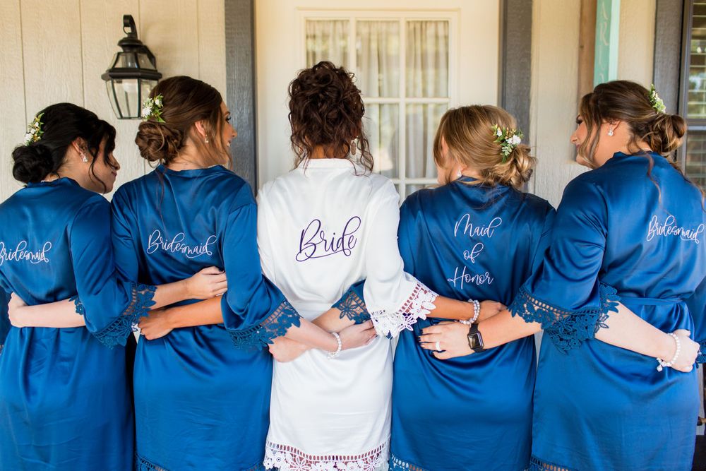 Matching blue robes worn by bridesmaids with bride in white robe showing their backs.