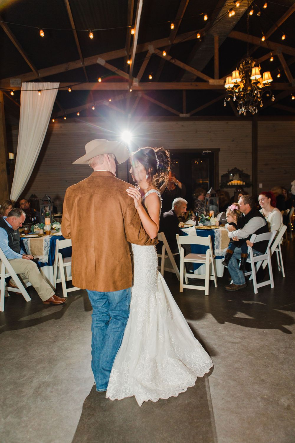 First dance moment captured under twinkling lights in rustic barn venue.