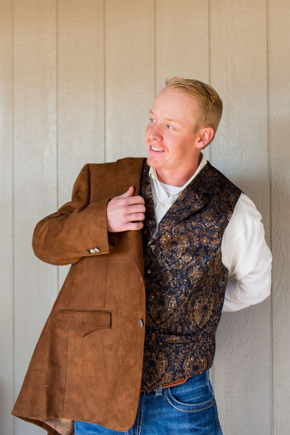 Person wearing brown jacket and patterned vest against beige wall.
