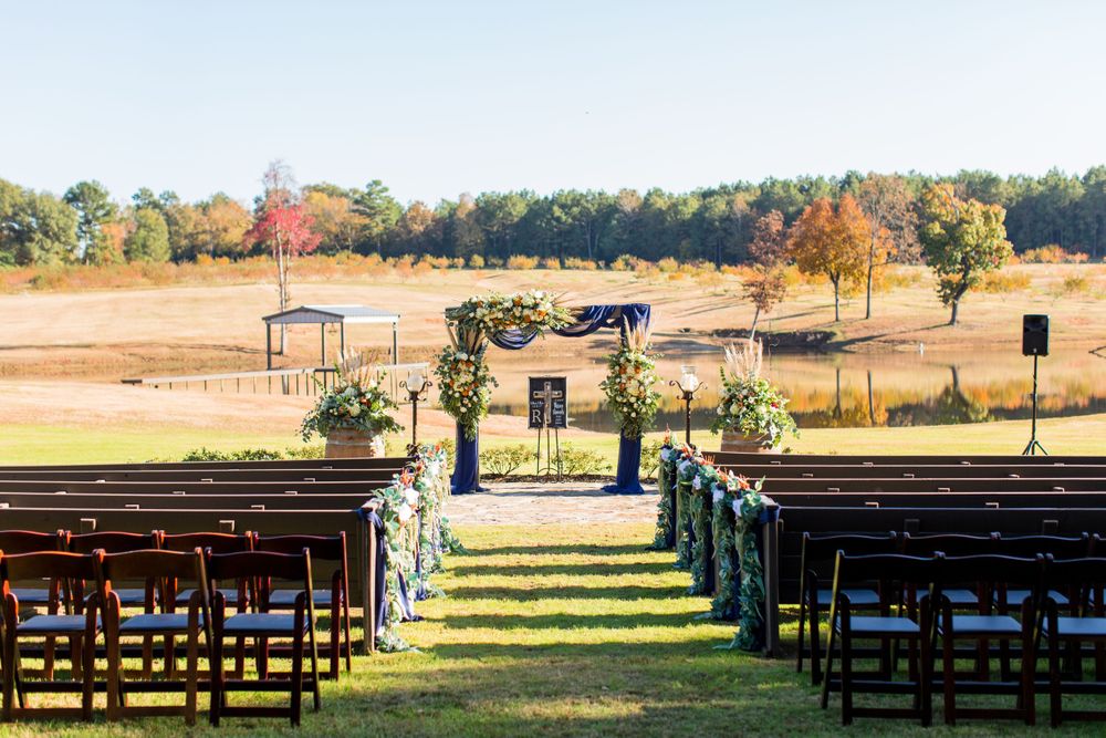 Outdoor wedding ceremony setup with wooden chairs facing decorated arch in autumn setting.