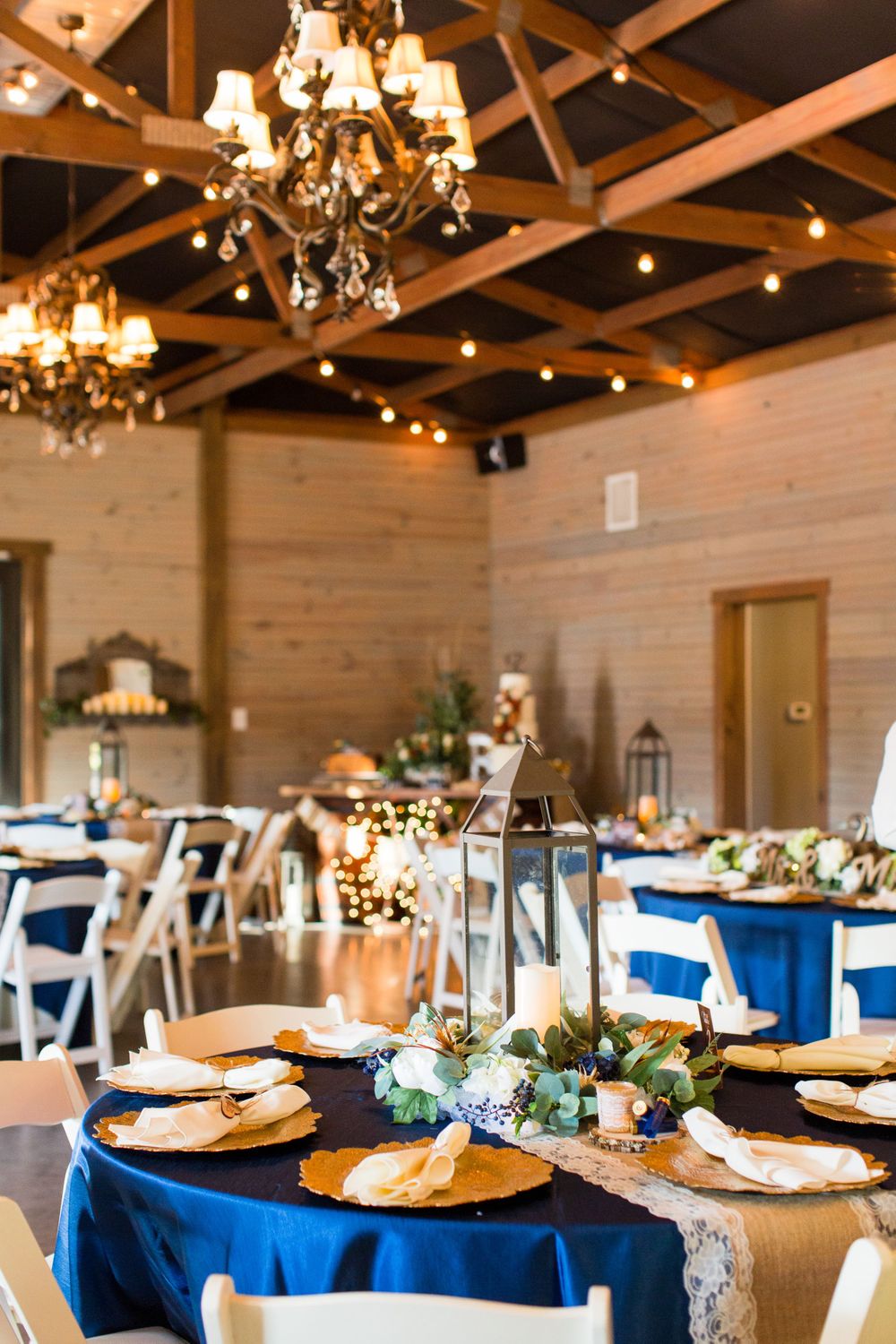 Elegant barn reception setup with navy linens, chandeliers, and string lights creating warm ambiance.
