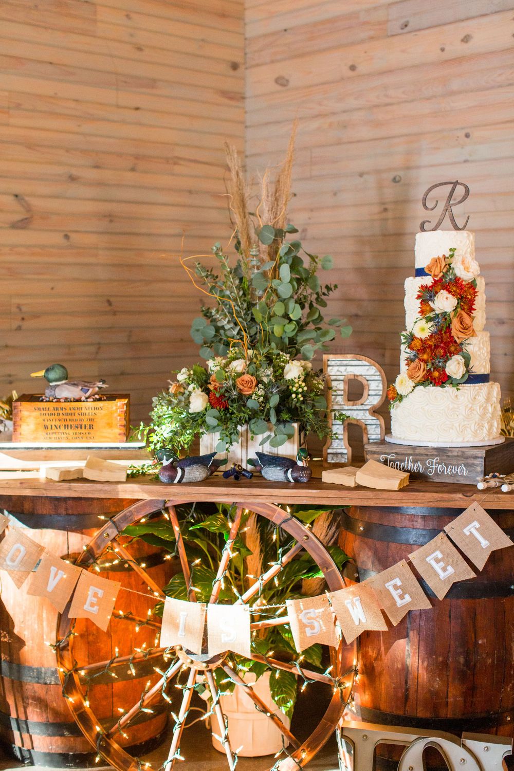 Rustic wedding dessert display with floral cake and decorations on wooden wheel barrel table.