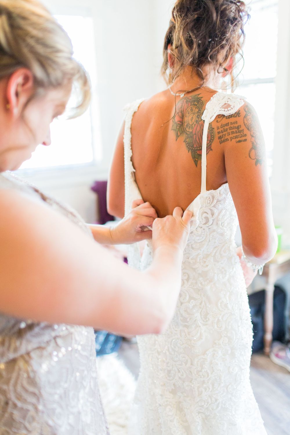 Helper assisting with the buttons on a detailed lace wedding dress.