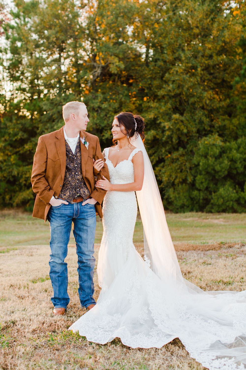 Couple shares intimate moment in outdoor fall setting with bride's lace gown trailing behind.