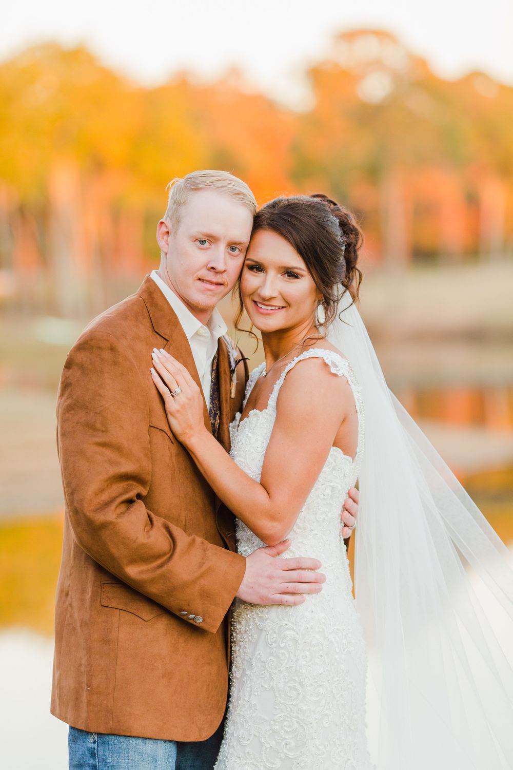 Newlyweds embrace during sunset portrait session with fall foliage in background.