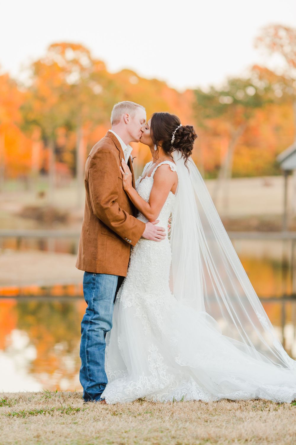 Romantic couple shares tender moment by lake with autumn colors reflecting in background.