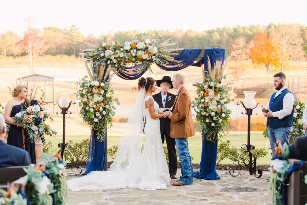 Outdoor wedding ceremony under an arch decorated with blue draping and white floral arrangements.