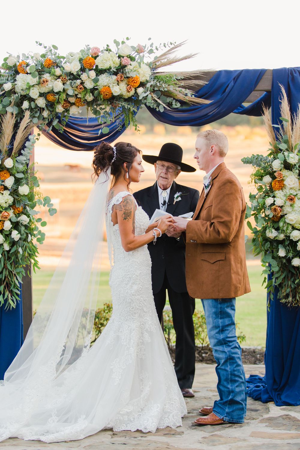 Beautiful wedding arch adorned with orange and white flowers and navy blue fabric during ceremony.
