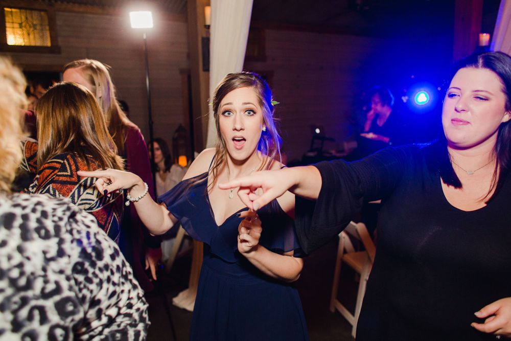 Wedding guests dance energetically on the reception dance floor with blue lighting.