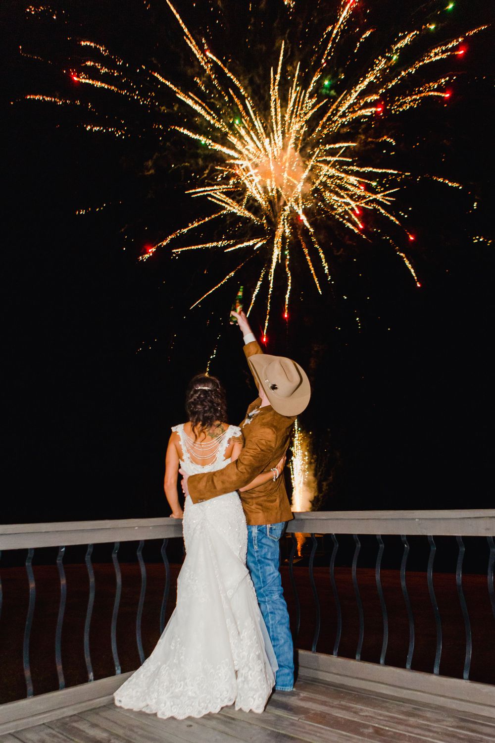 Couple watching fireworks display from a wooden deck during a celebration.